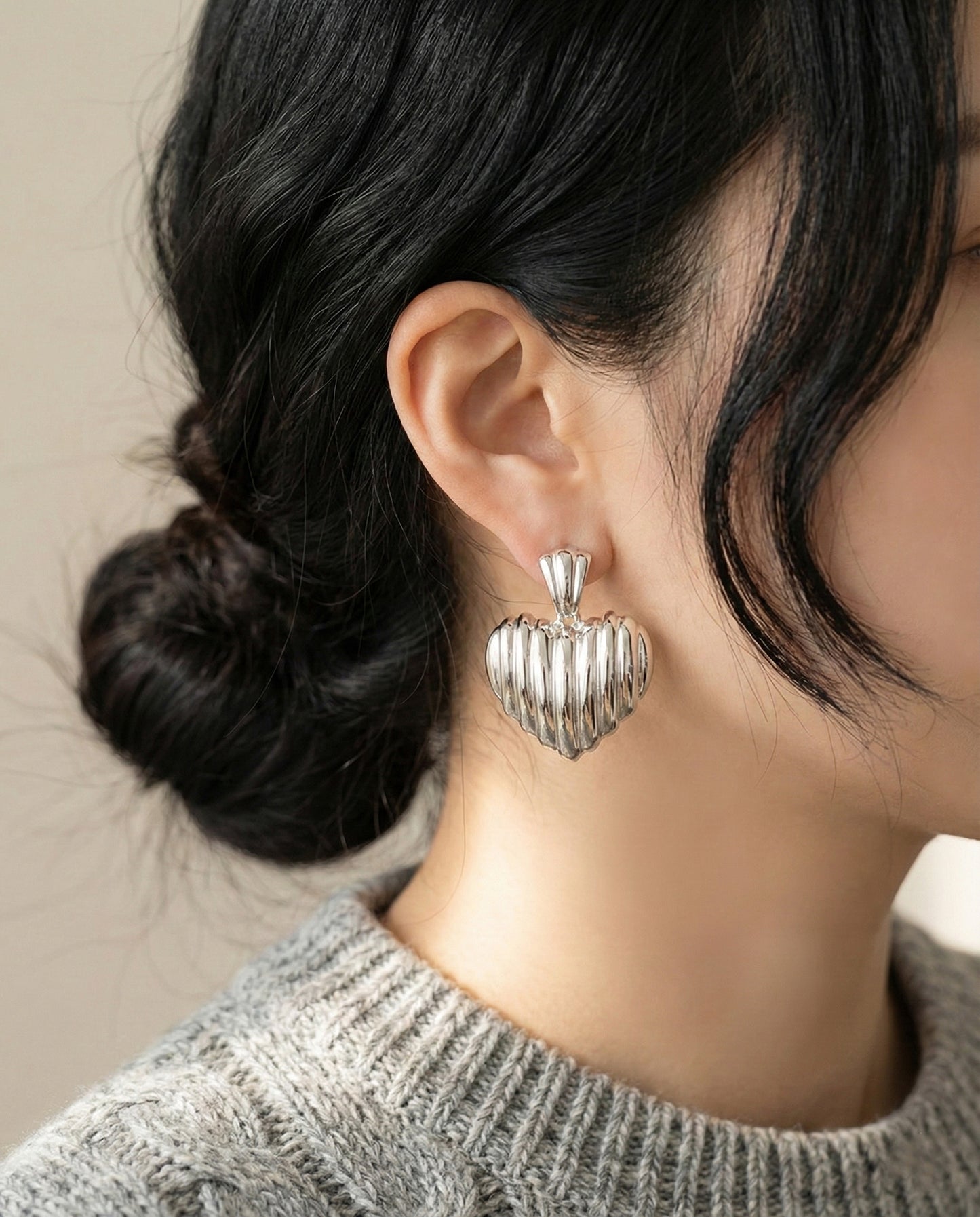 Model wearing silver ribbed heart earrings with grey knit sweater side view