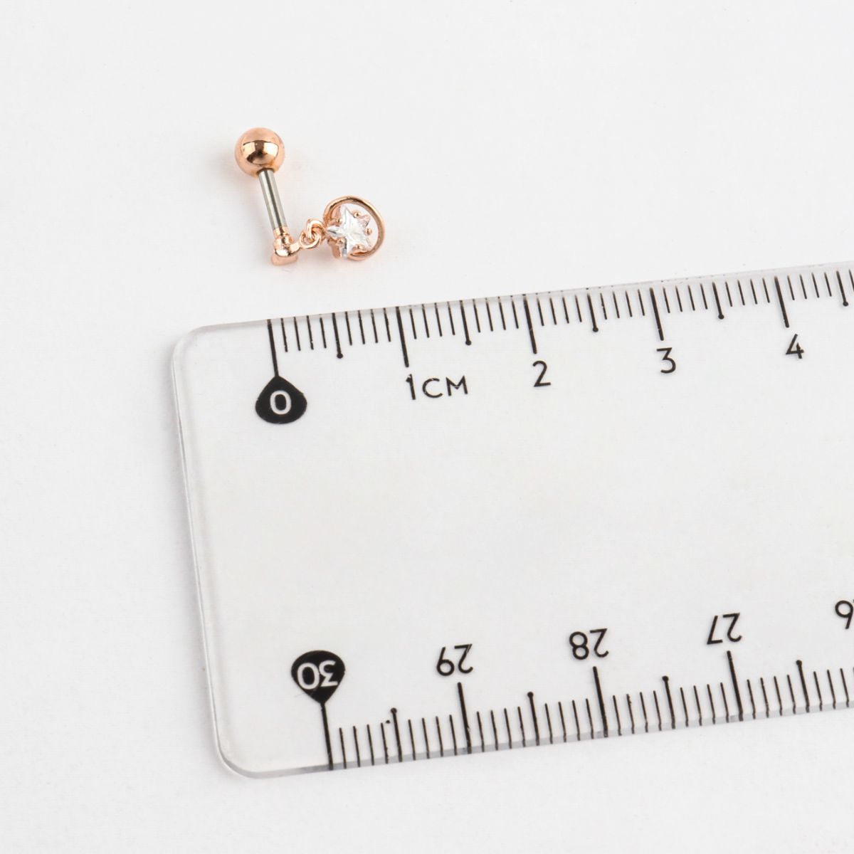 Gold and blue planet barbell earring placed next to a transparent ruler for size reference.