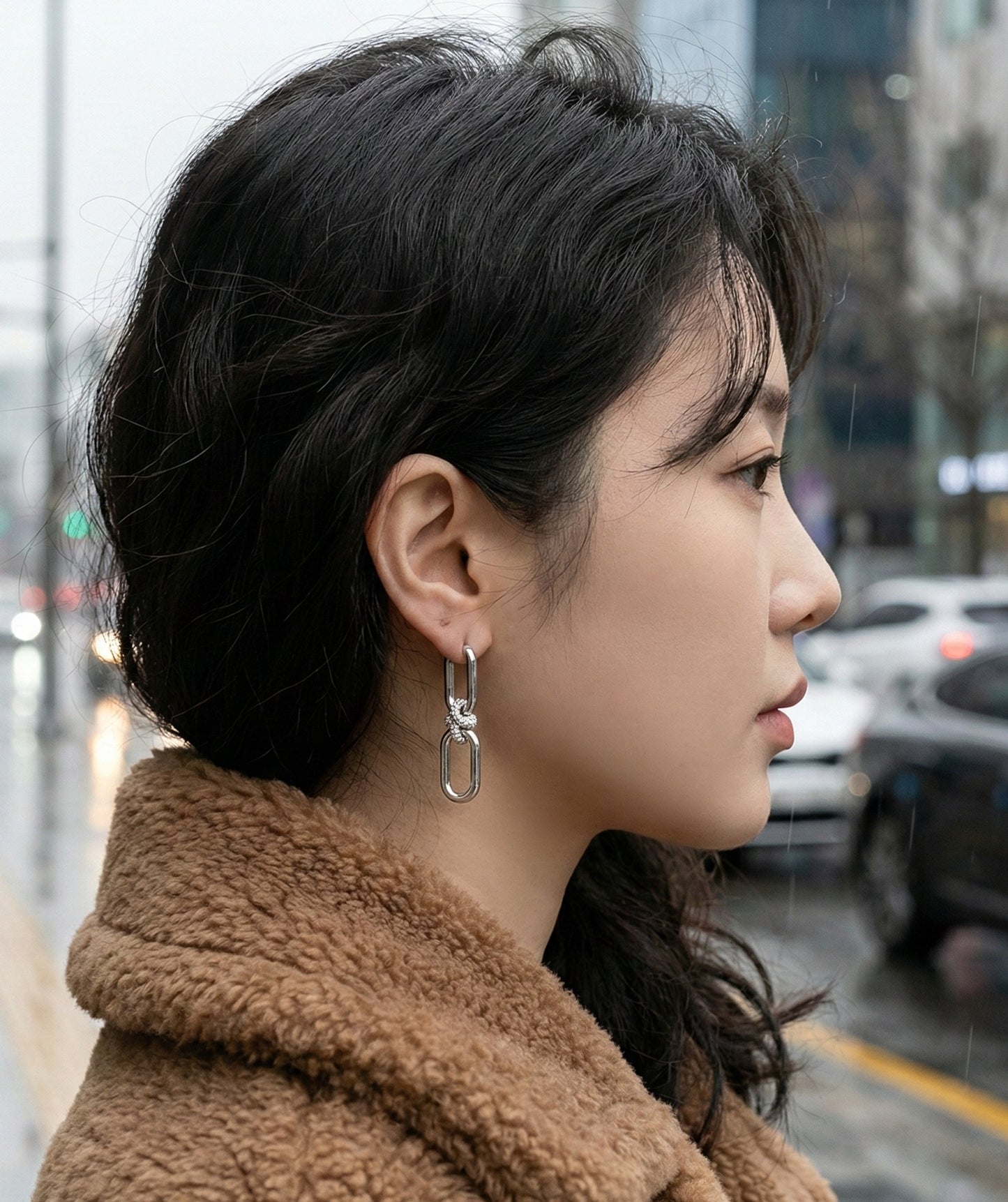 Close-up side view of silver chain link earrings with pavé crystal knot, casual street style