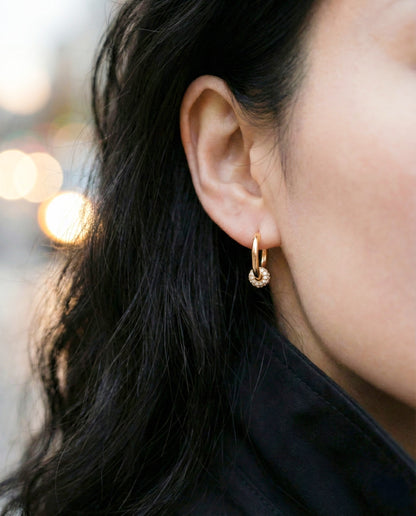 Woman wearing gold pave huggie earrings street style black coat