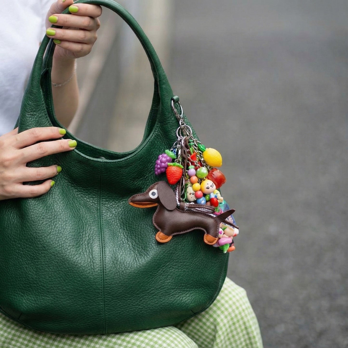 Brown leather Dachshund purse charm with colorful fruit charms and beaded decorations on green handbag