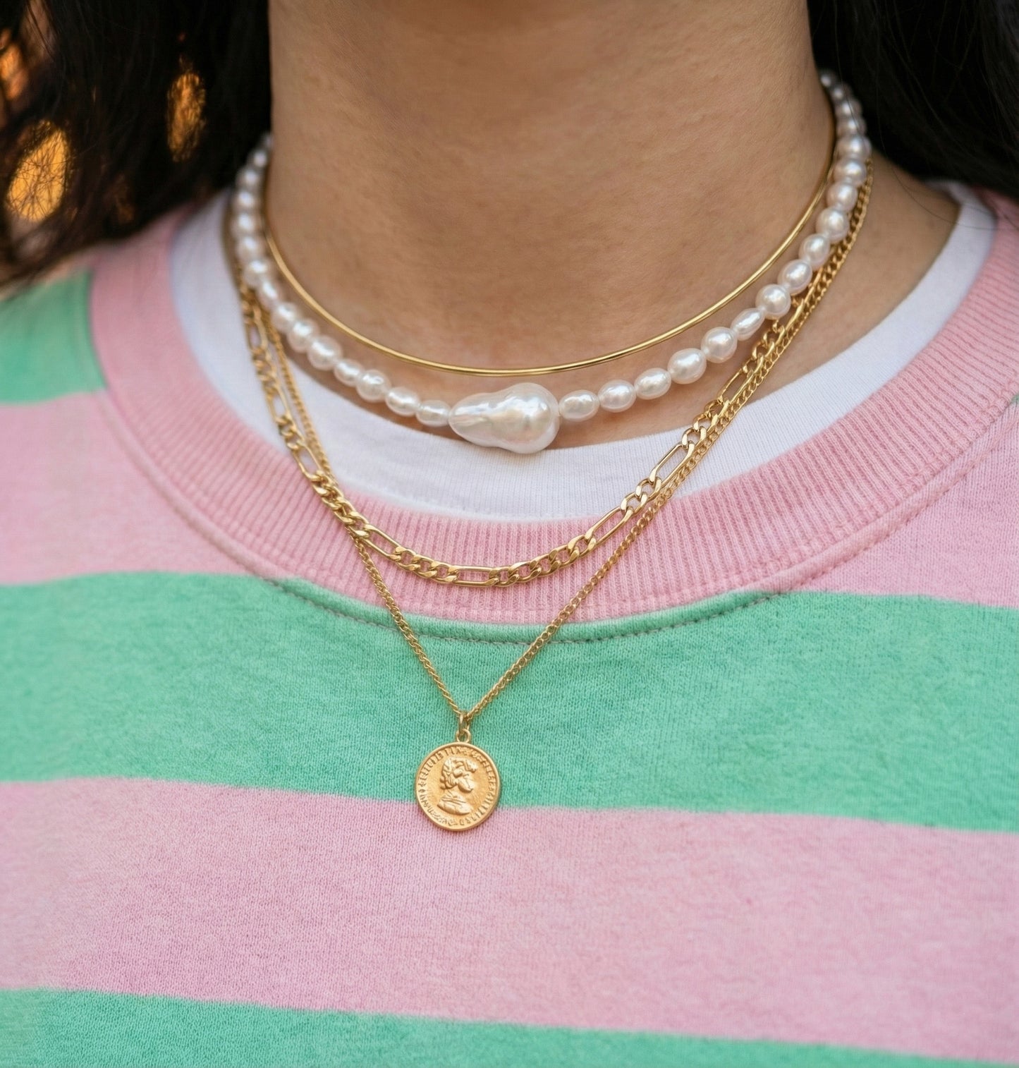 Gold freshwater pearl choker layered with chain necklaces on striped pink sweater