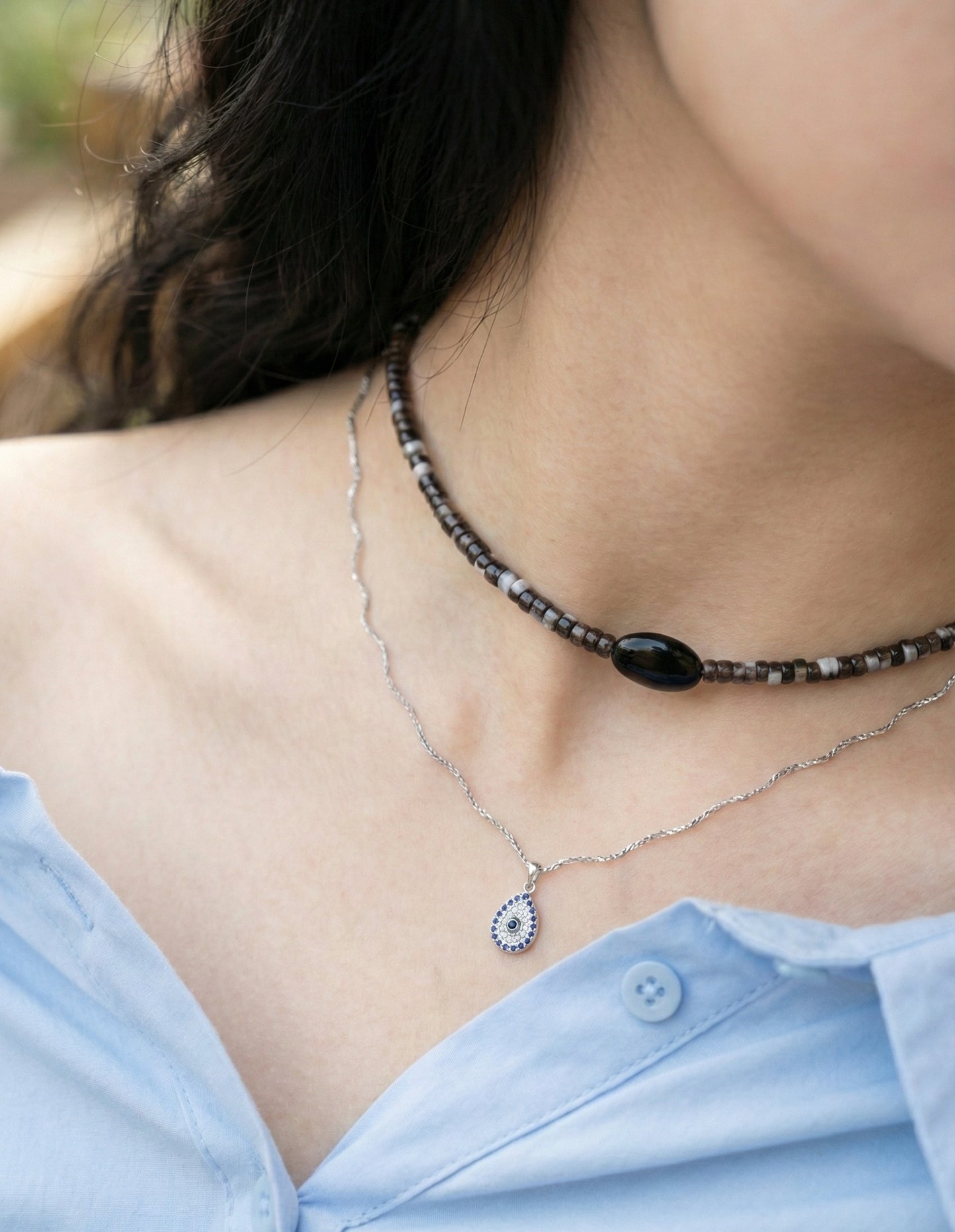 Woman wearing black onyx choker layered with silver necklaces and blue shirt