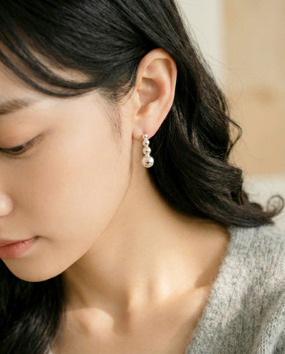 Silver graduated ball bar earrings worn with gray cardigan sweater