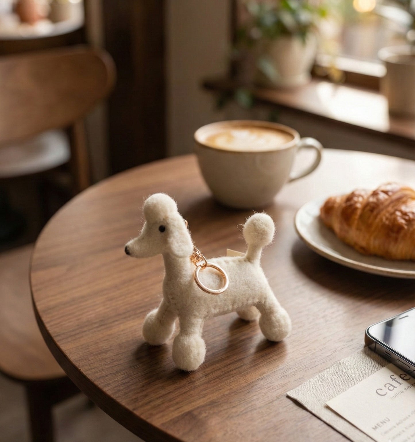 White cream poodle keychain on wooden cafe table with latte and croissant, soft natural lighting