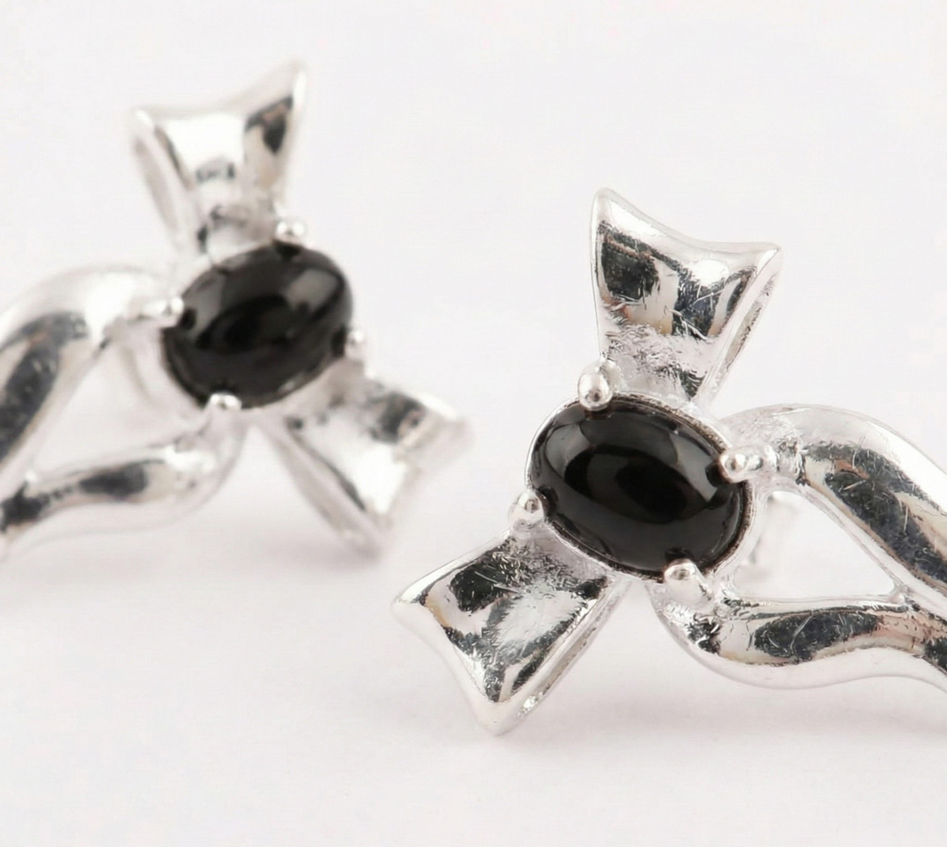 Macro close-up of black agate oval cabochon set in 925 sterling silver bow earring — 4-prong setting detail shot