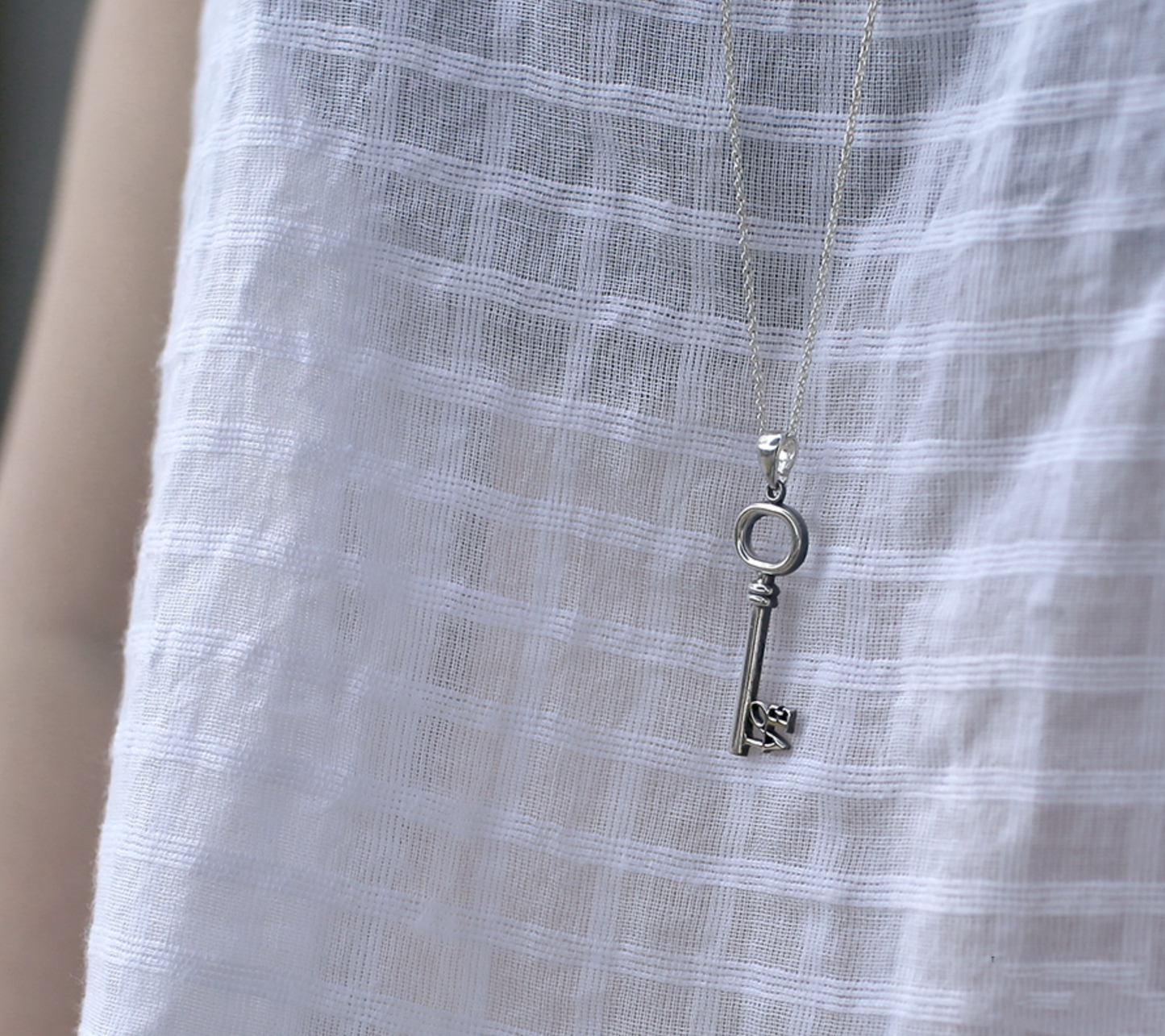  Side angle of the key pendant against a white textured fabric, highlighting its metallic luster. 