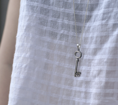  Side angle of the key pendant against a white textured fabric, highlighting its metallic luster. 