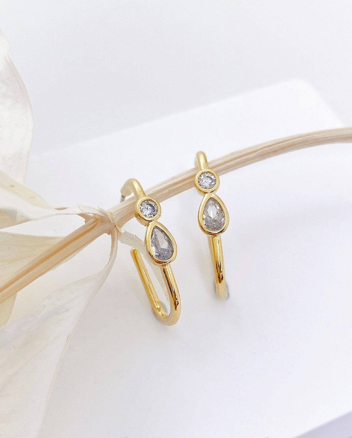 Close-up detail of gold bezel-set teardrop pear-cut and round CZ stones on brass hoop earring