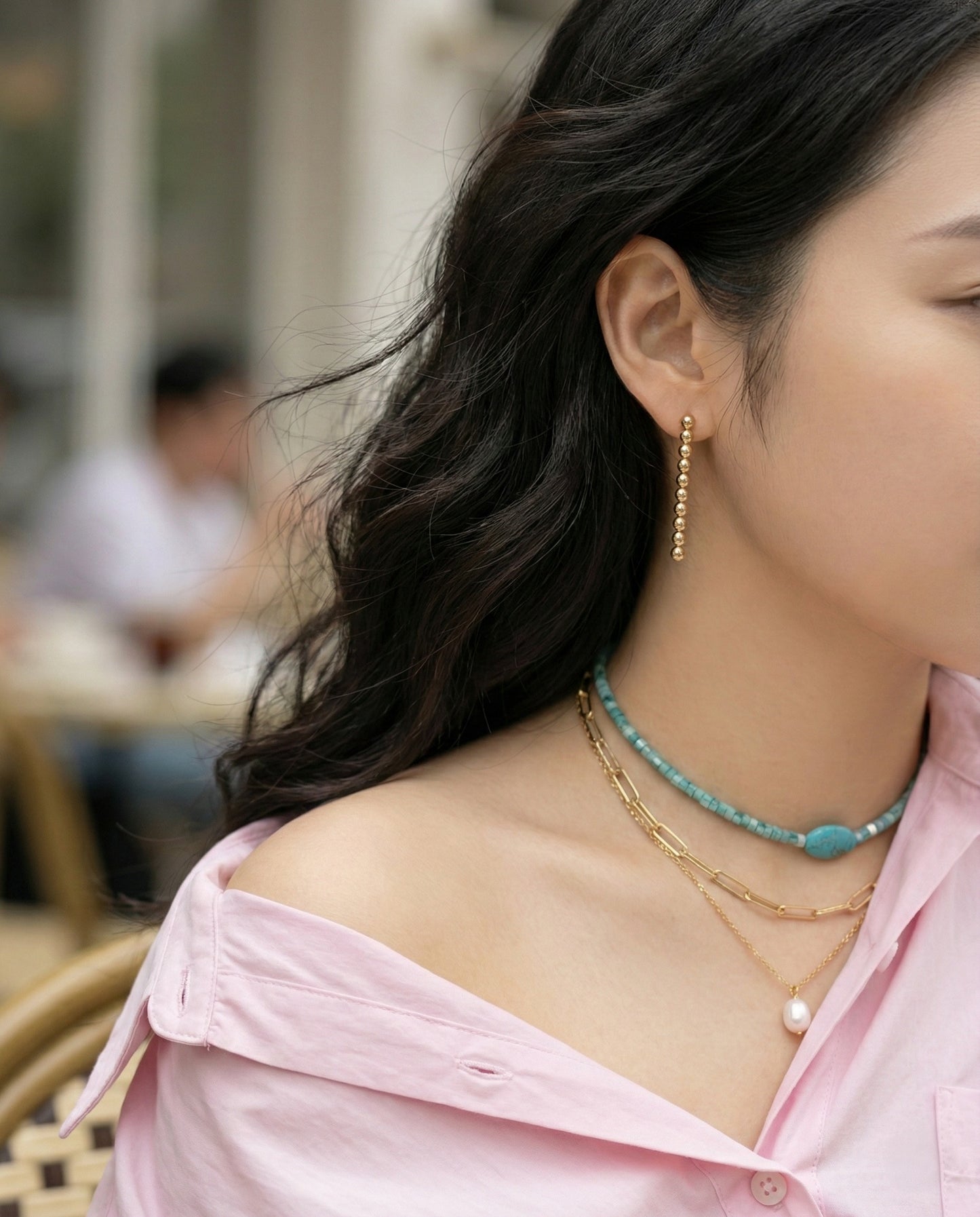 Side view of woman wearing gold ball drop earrings with turquoise necklace