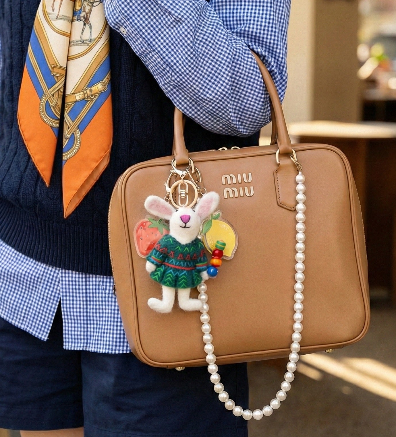 Full view of person carrying tan Miu Miu bag decorated with wool felt rabbit charm and pearl strand