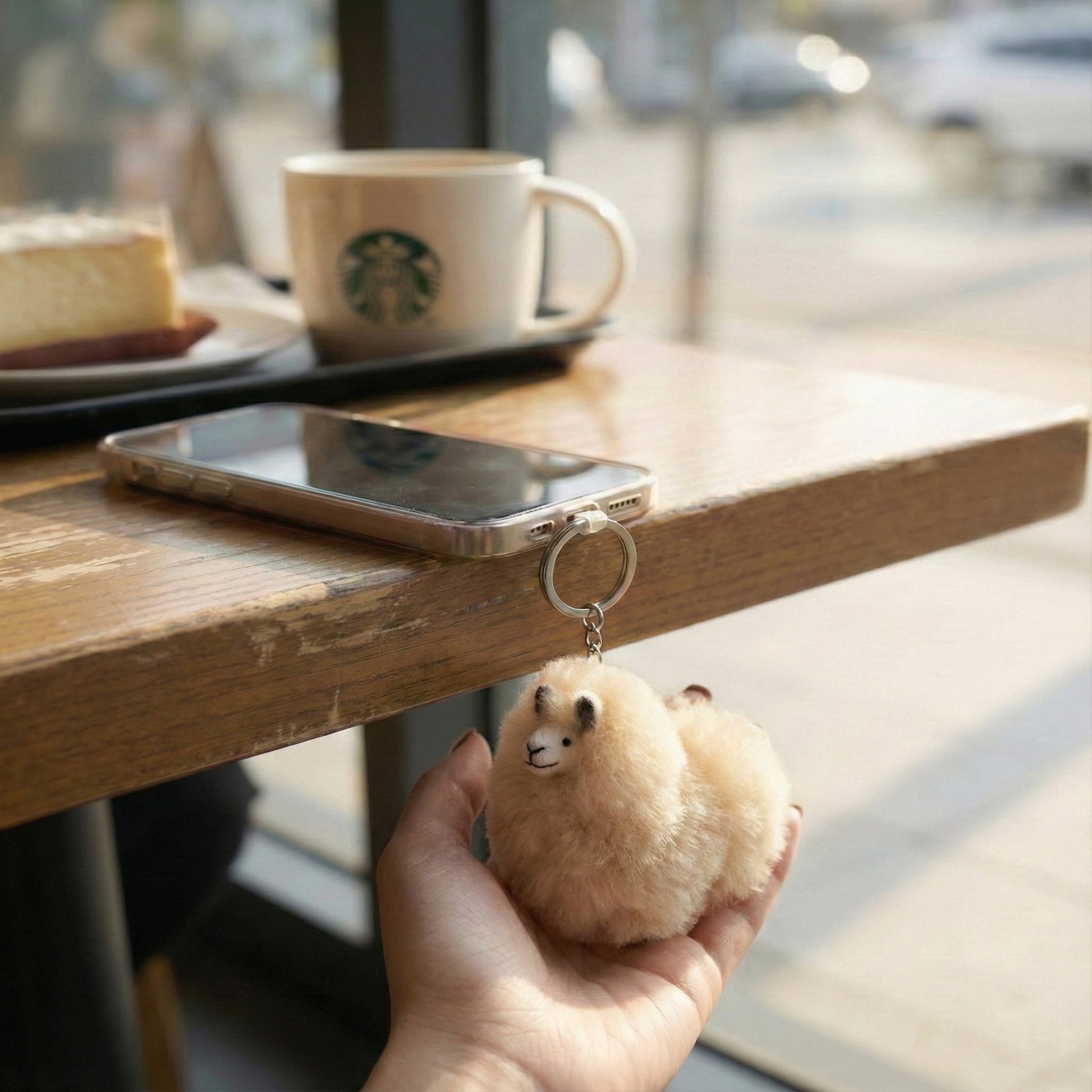 Hand holding fluffy beige alpaca keychain at café setting