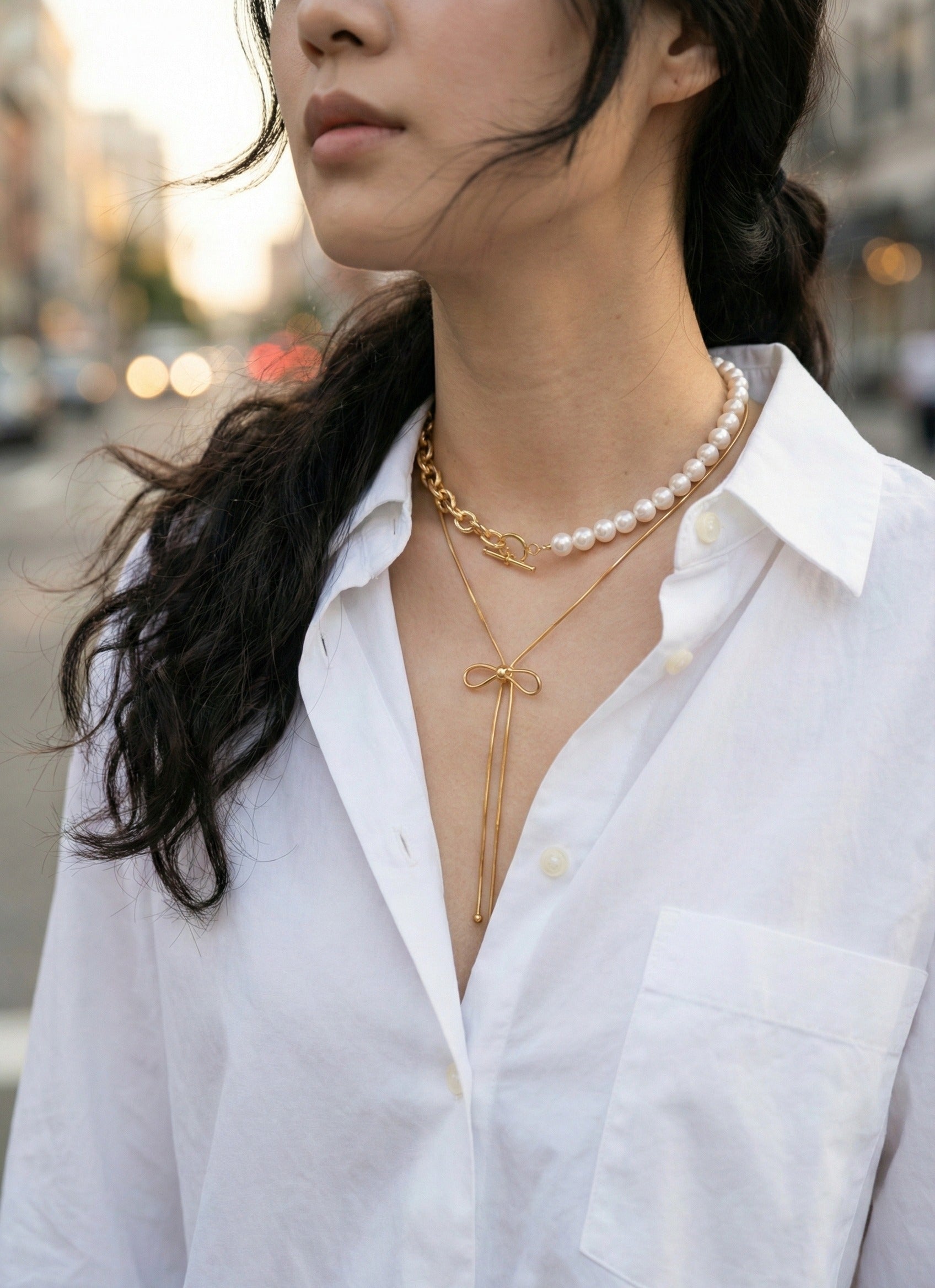 Gold ribbon bow necklace styled with white blouse and pearl choker - romantic layering