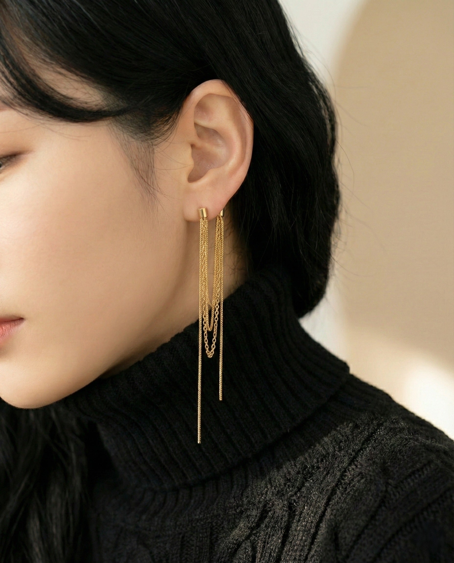 Close up of gold layered tassel chain earrings on model with black knit sweater