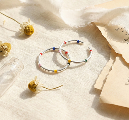 Flat lay of two 925 sterling silver multicolor enamel open rings with dried flowers and vintage book pages, lifestyle product photography