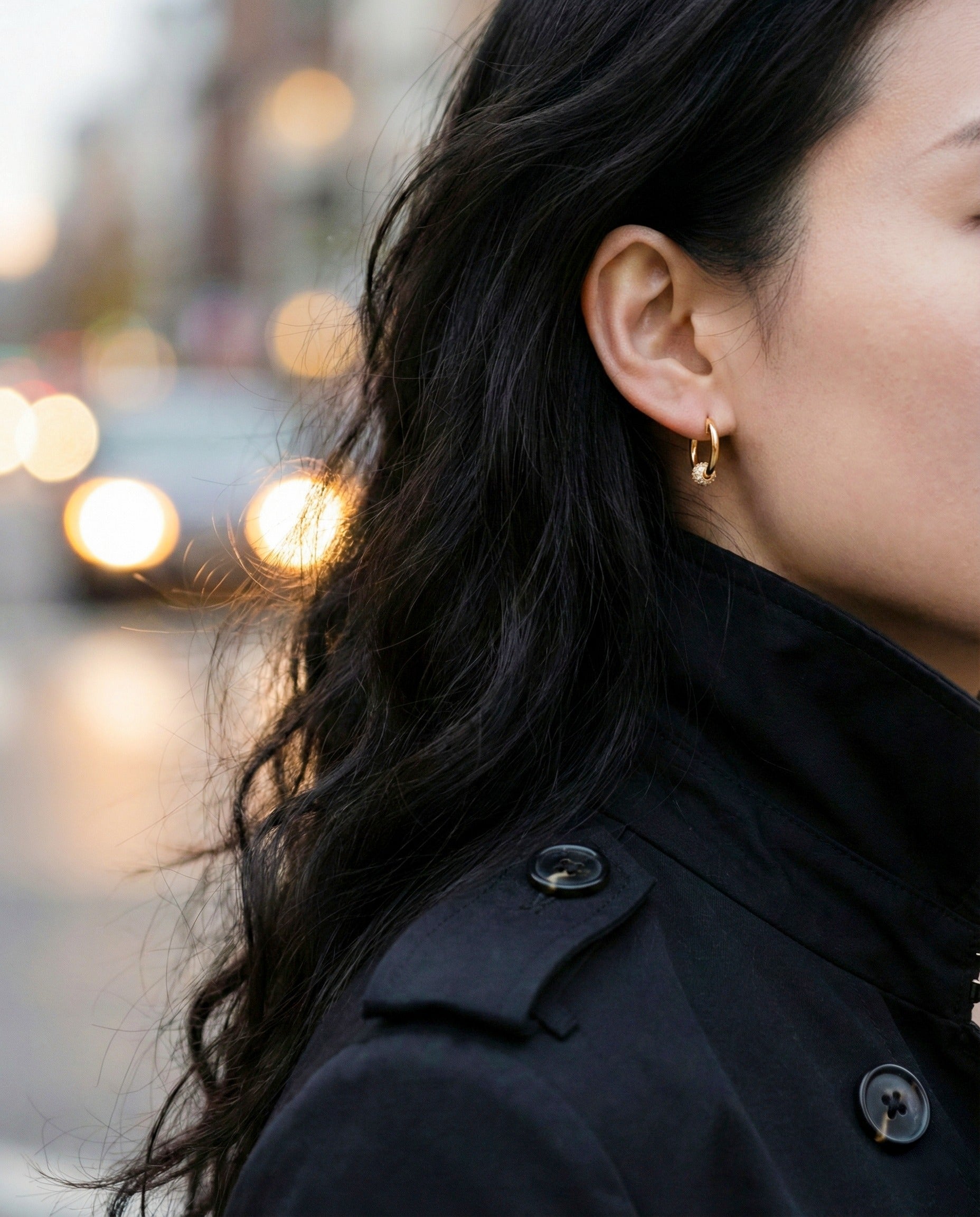 Elegant gold huggie hoop earrings worn with black outfit bokeh background