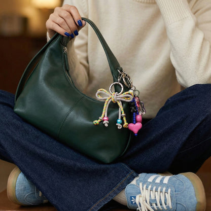 Woman in cream sweater holding green hobo bag with pink rhinestone bow charm close-up