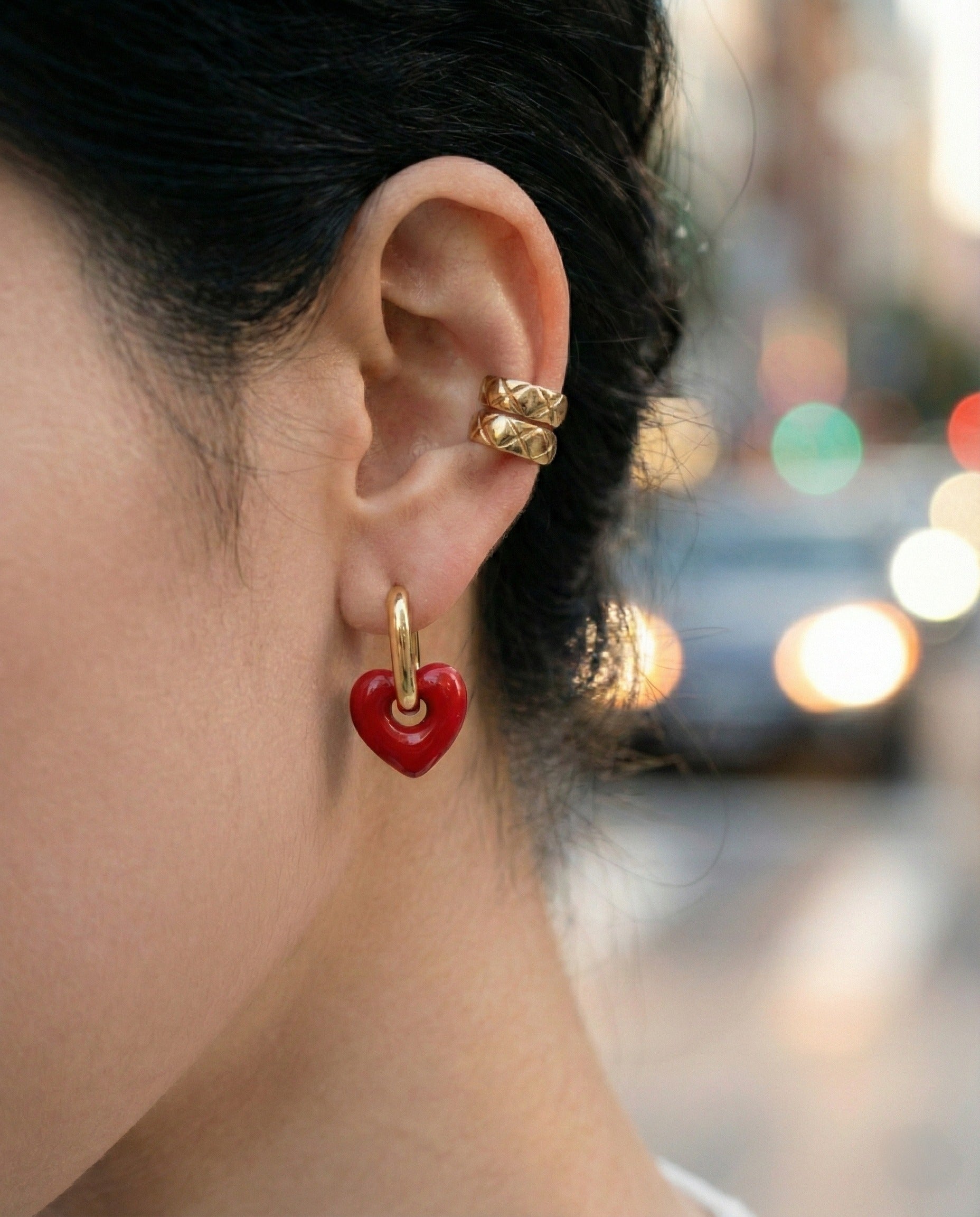 Woman wearing red puffy heart huggie earrings with white knit sweater, side view showing ear styling