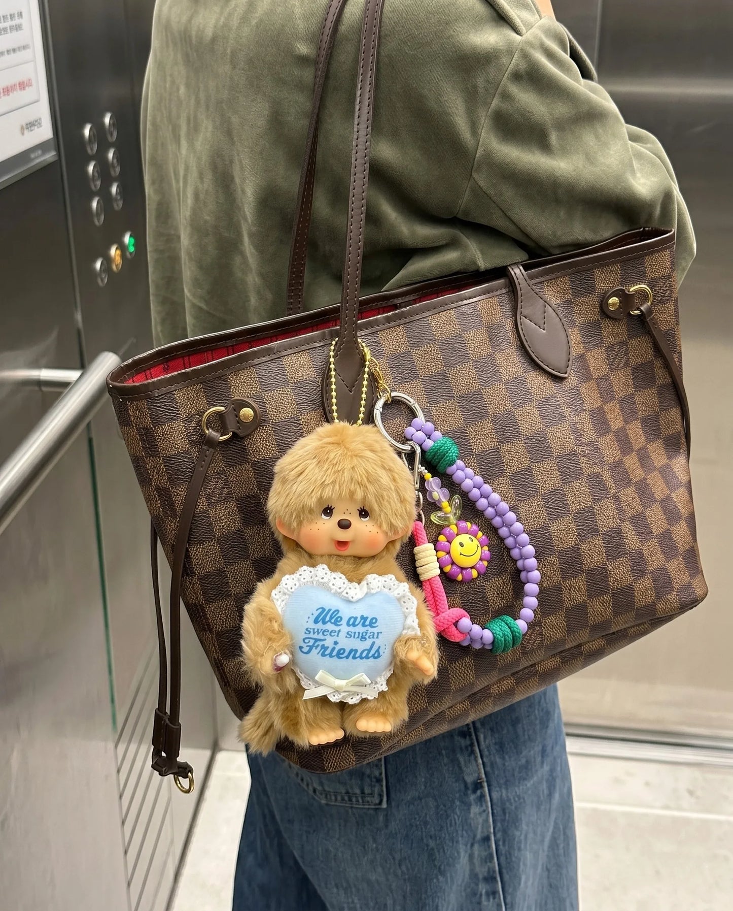 Y2K bag charm layered look 8ttitto8 lavender smiley flower bead strap with Monchhichi on Louis Vuitton Neverfull, elevator street shot.
