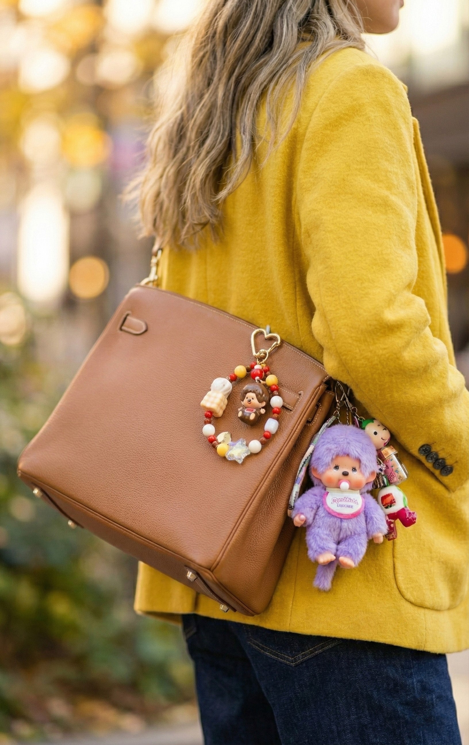 Woman wearing yellow cardigan with brown bag decorated with Monchhichi beaded keychain bag charm, autumn outdoor setting