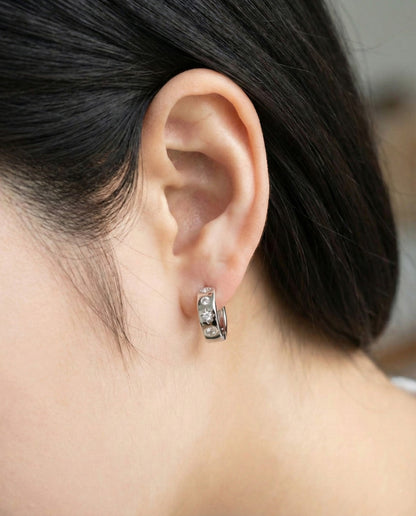 Close-up of silver hoop earrings with celestial star engravings and stones, worn on left ear.