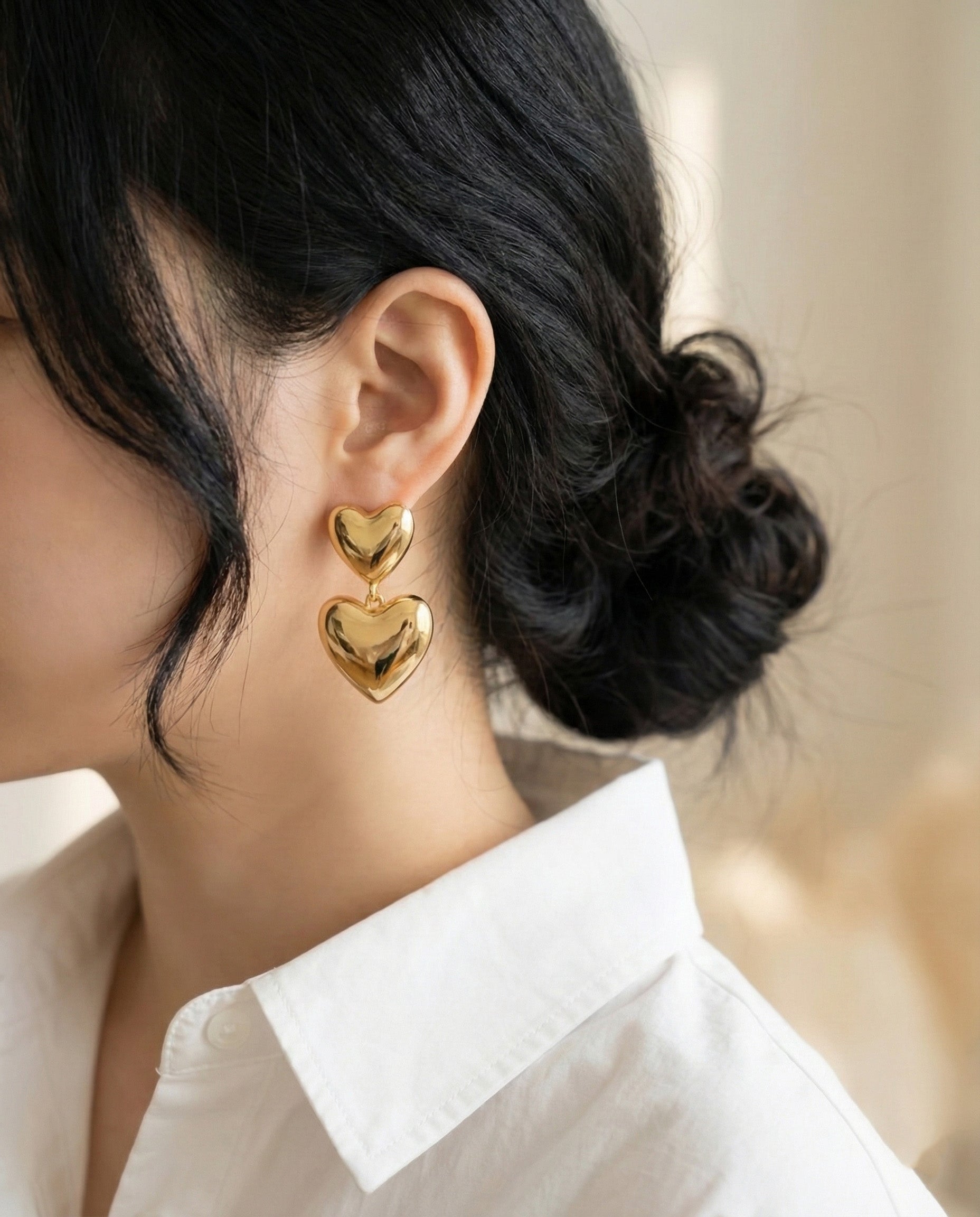 Model wearing gold chunky heart earrings with white shirt - elegant styling