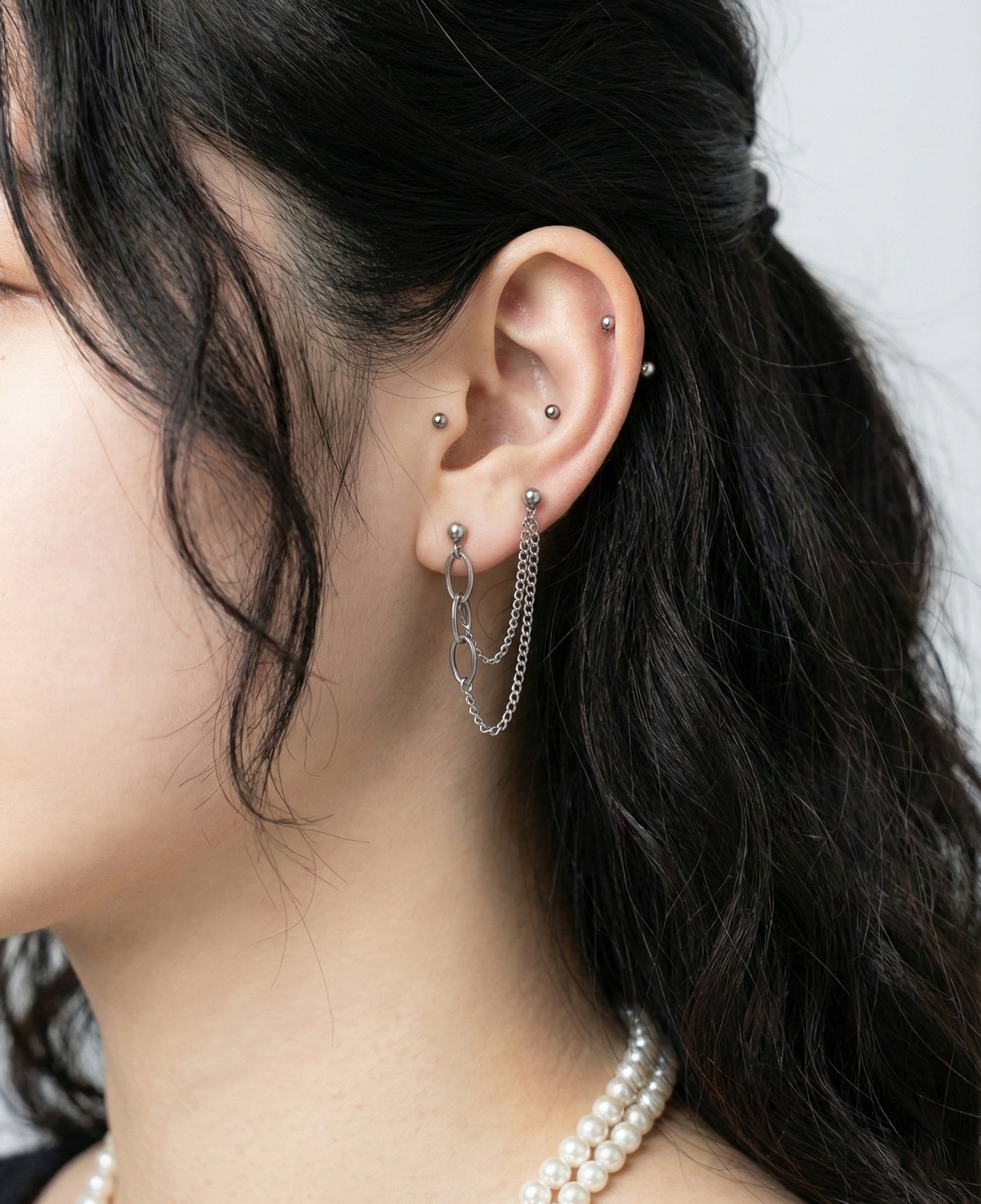 Multiple piercing styling with connected chain barbell and small stud earrings for curated ear stack"