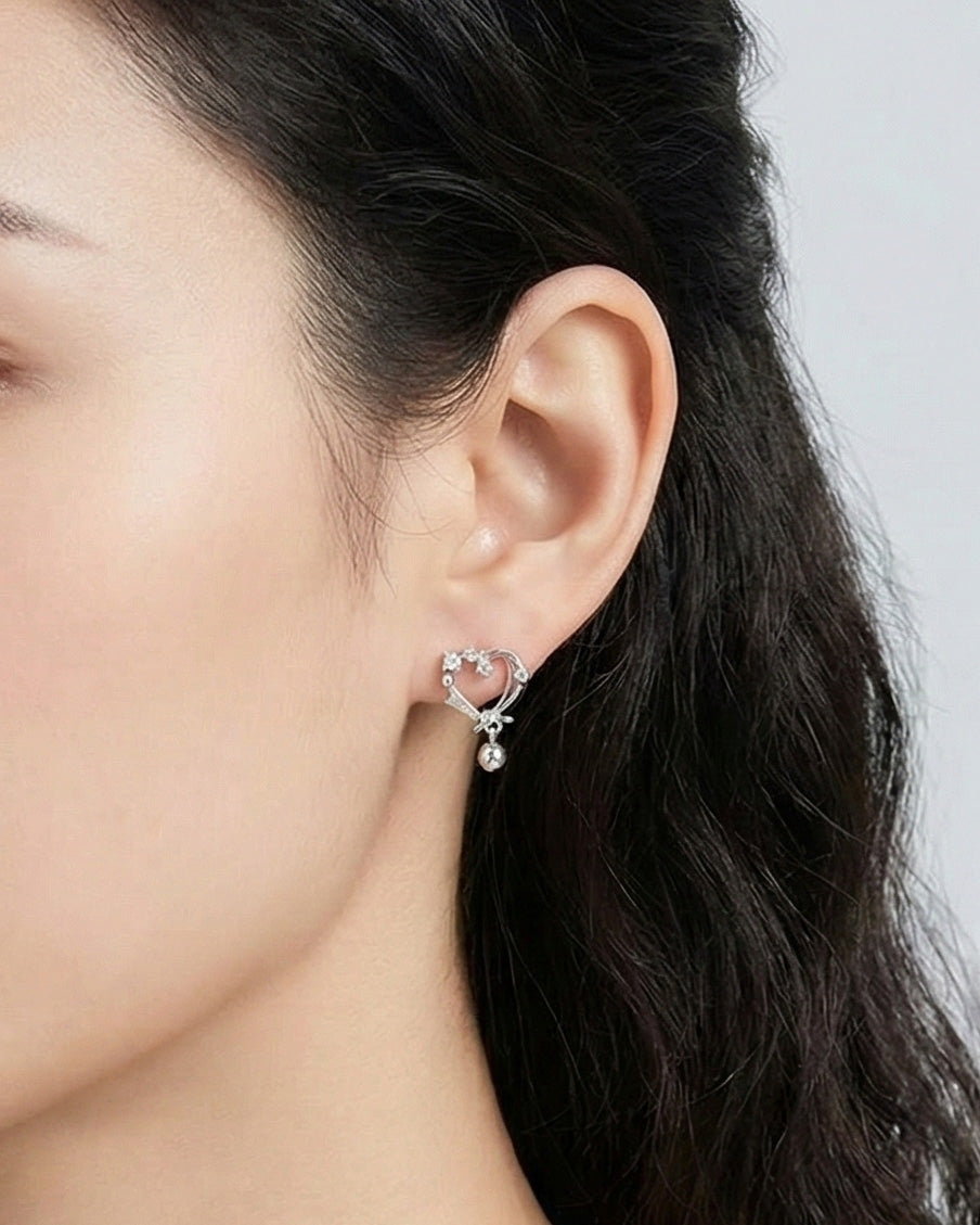 Close-up side profile of woman wearing silver heart earrings with crystal accents and teardrop charm, delicate dainty design for sensitive ears, hypoallergenic 925 posts
