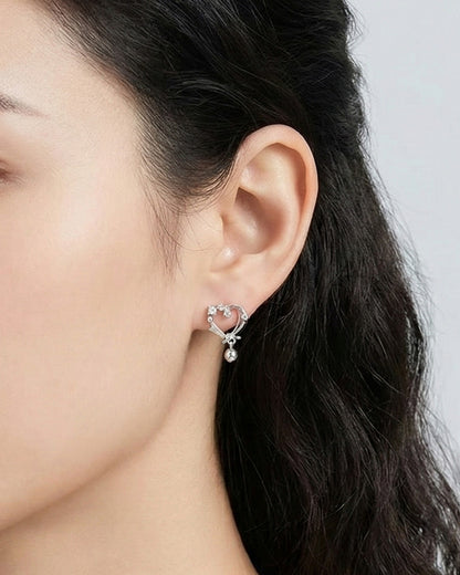 Close-up side profile of woman wearing silver heart earrings with crystal accents and teardrop charm, delicate dainty design for sensitive ears, hypoallergenic 925 posts