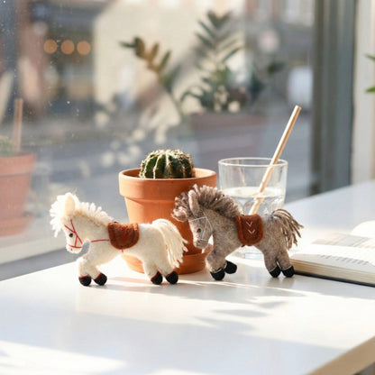 White and grey wool felt horse charms displayed on cafe table with cactus plant and glass