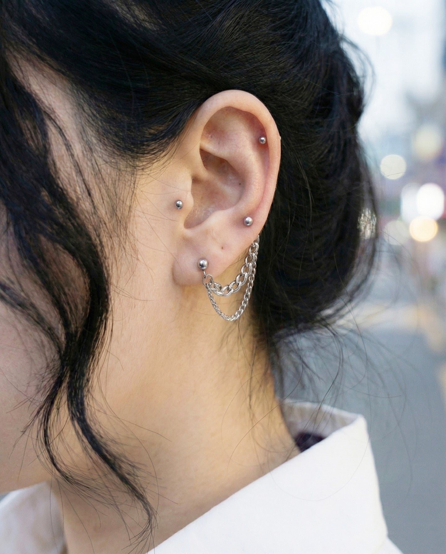 Close-up of two-pin chain connected piercing worn on lobe, black sweater styling