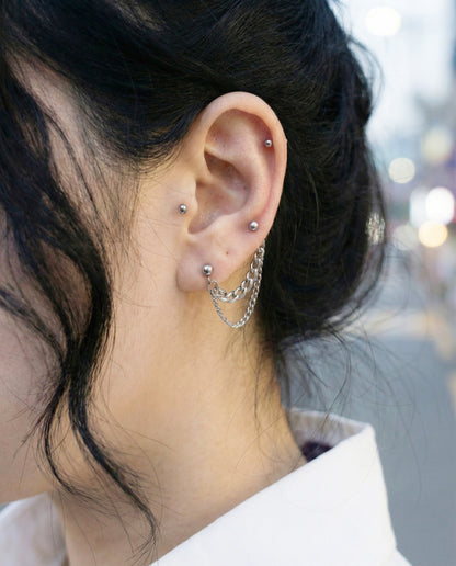 Close-up of two-pin chain connected piercing worn on lobe, black sweater styling