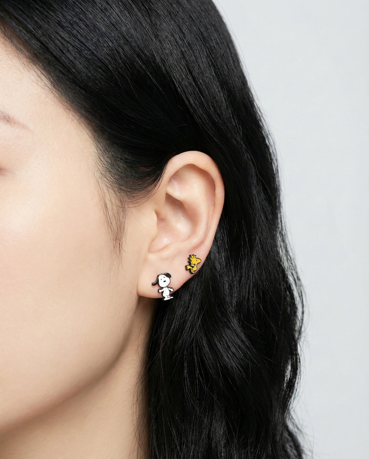 Close-up of a person wearing two different pairs of earrings on a plain background