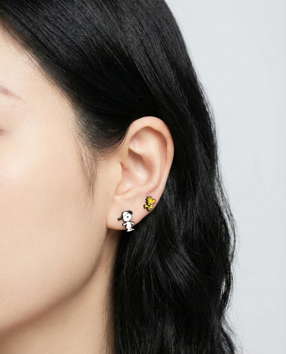 Close-up of a person wearing two different pairs of earrings on a plain background