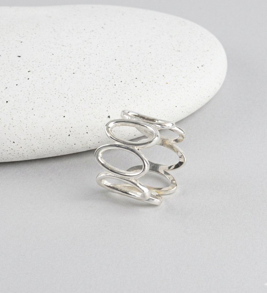 925 sterling silver oval loop wide band ring propped against white speckled stone on gray surface, showing open oval link structure and polished finish