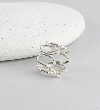 925 sterling silver oval loop wide band ring propped against white speckled stone on gray surface, showing open oval link structure and polished finish