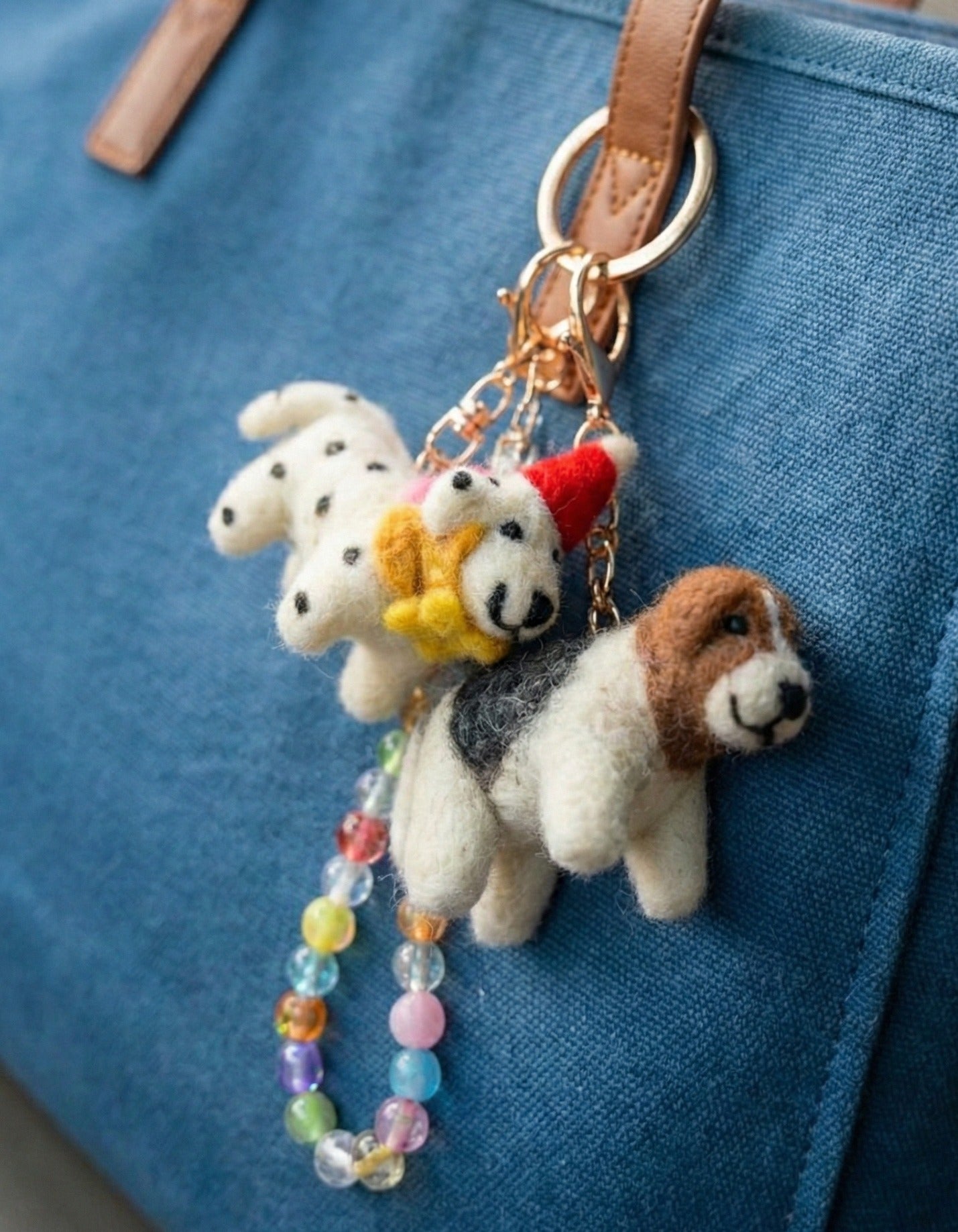 Close-up of felt dog keychains on blue canvas bag with gold hardware and rainbow bead strand