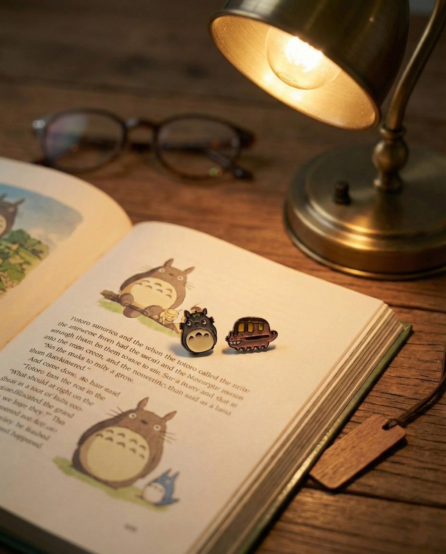 Totoro and Catbus stud earrings on open Studio Ghibli storybook with warm desk lamp