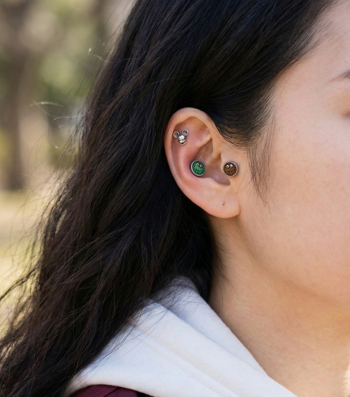 Side profile ear curation showing brown and green Oreo piercings on helix and lobe with Mickey on conch
