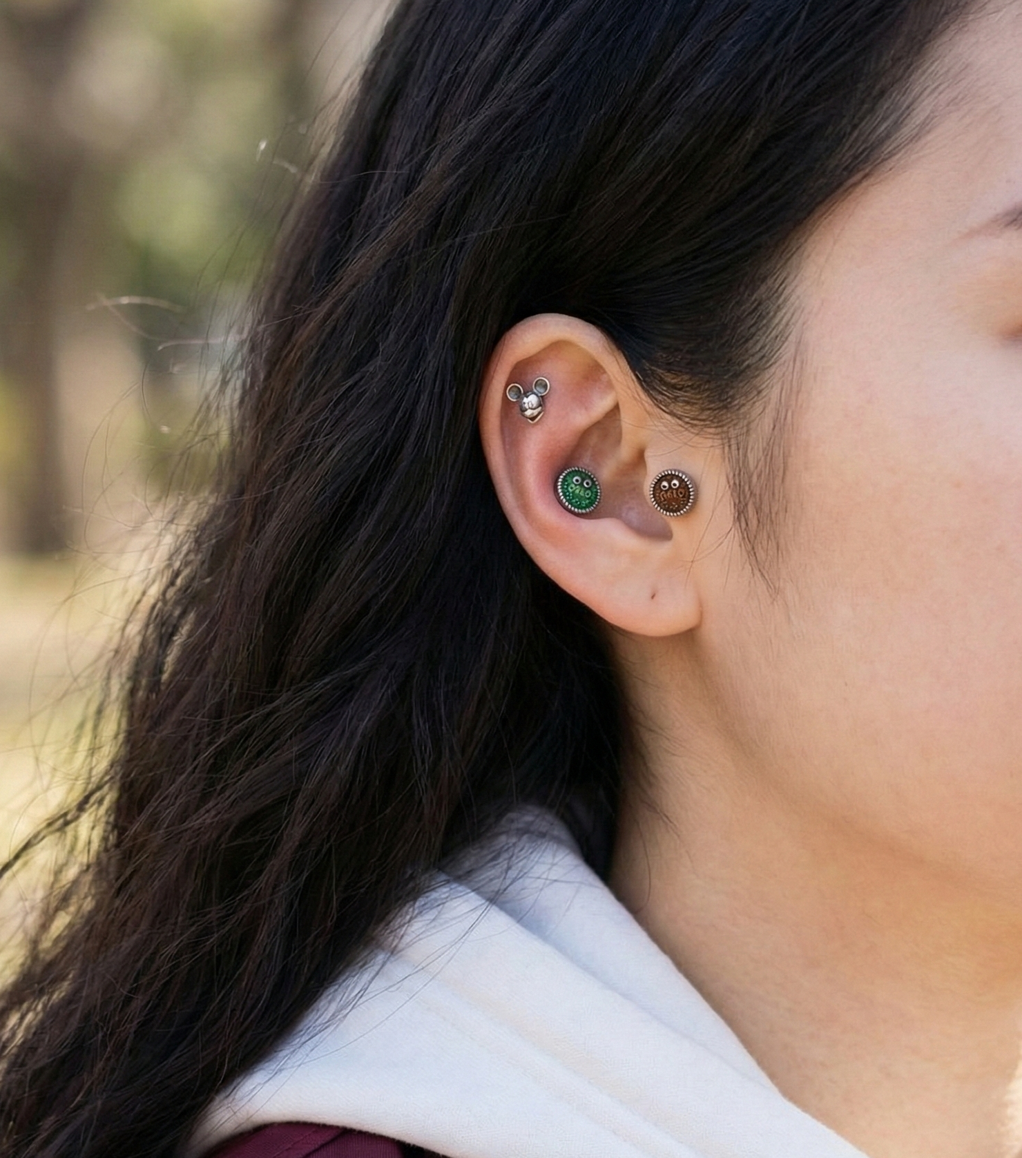 Side profile ear curation showing brown and green Oreo piercings on helix and lobe with Mickey on conch