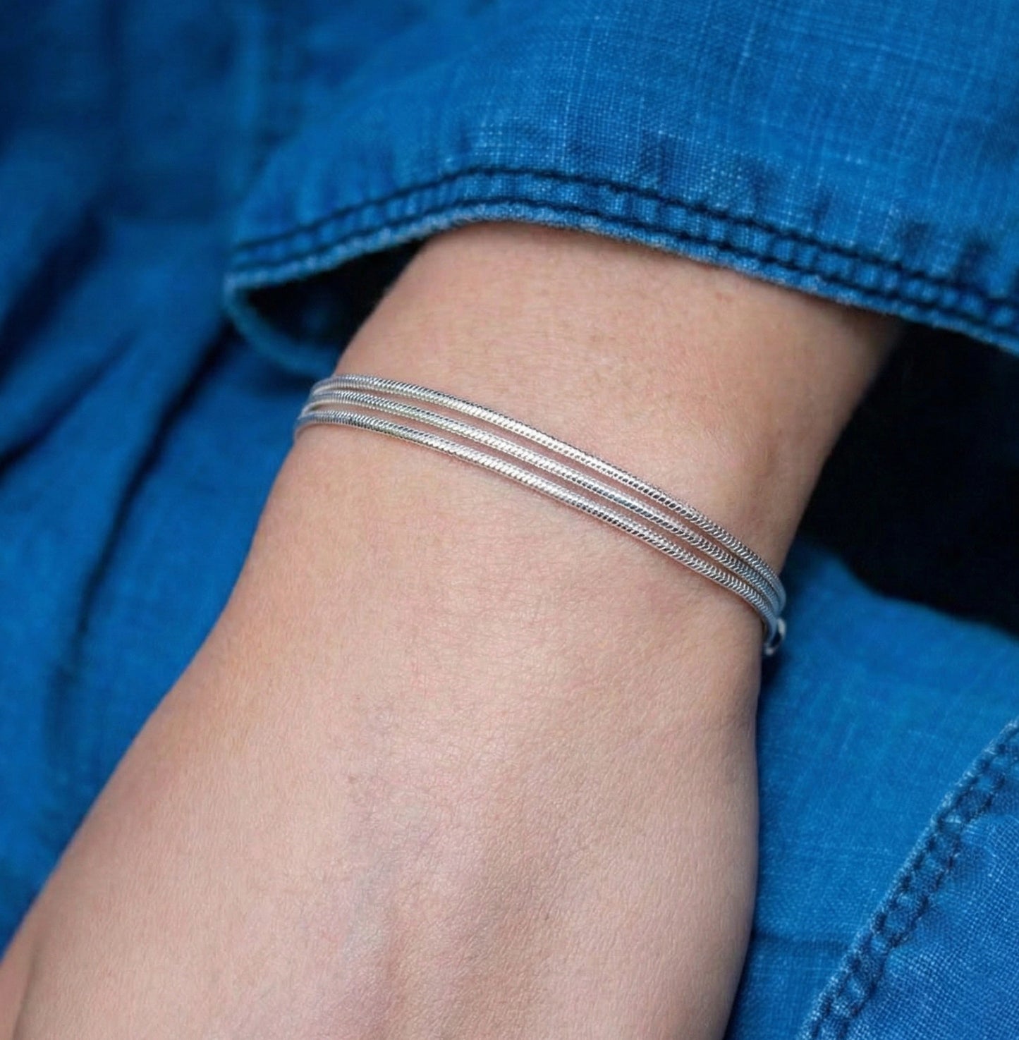 Sterling silver 3-strand snake chain bracelet worn on wrist over denim jeans – casual layered look