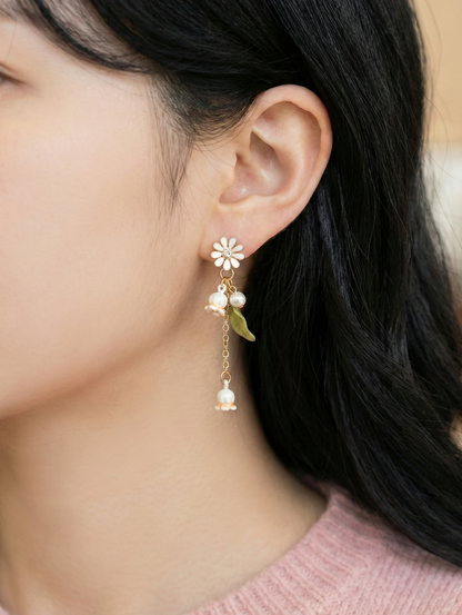 Woman modeling the white botanical drop earring with a green leaf detail.