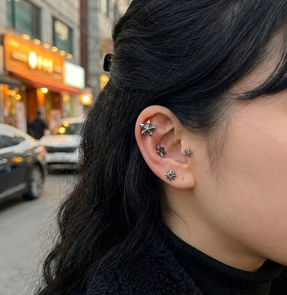 Model wearing all four vintage star barbell piercings in an ear stacking look from helix to lobe on city street