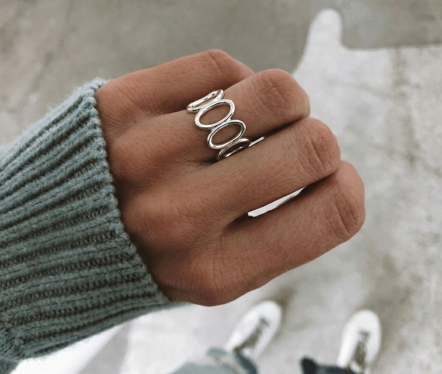 Sterling silver oval loop wide band ring worn on index finger, teal ribbed knit sleeve, casual outdoor setting, modern sculptural ring detail