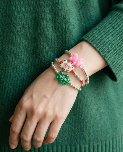 Three Hug Me bear bracelets layered on wrist wearing green knit sweater — pink, white, green gummy bears stacked