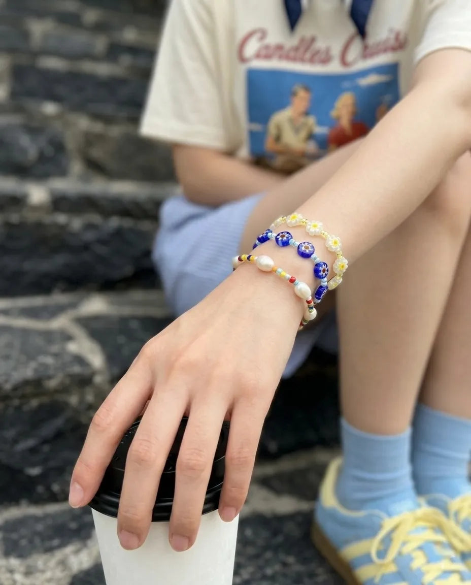 Clean girl summer wrist stack — apple green and sky blue Millefiori flower bead bracelets layered, linen blazer off-shoulder vibe.