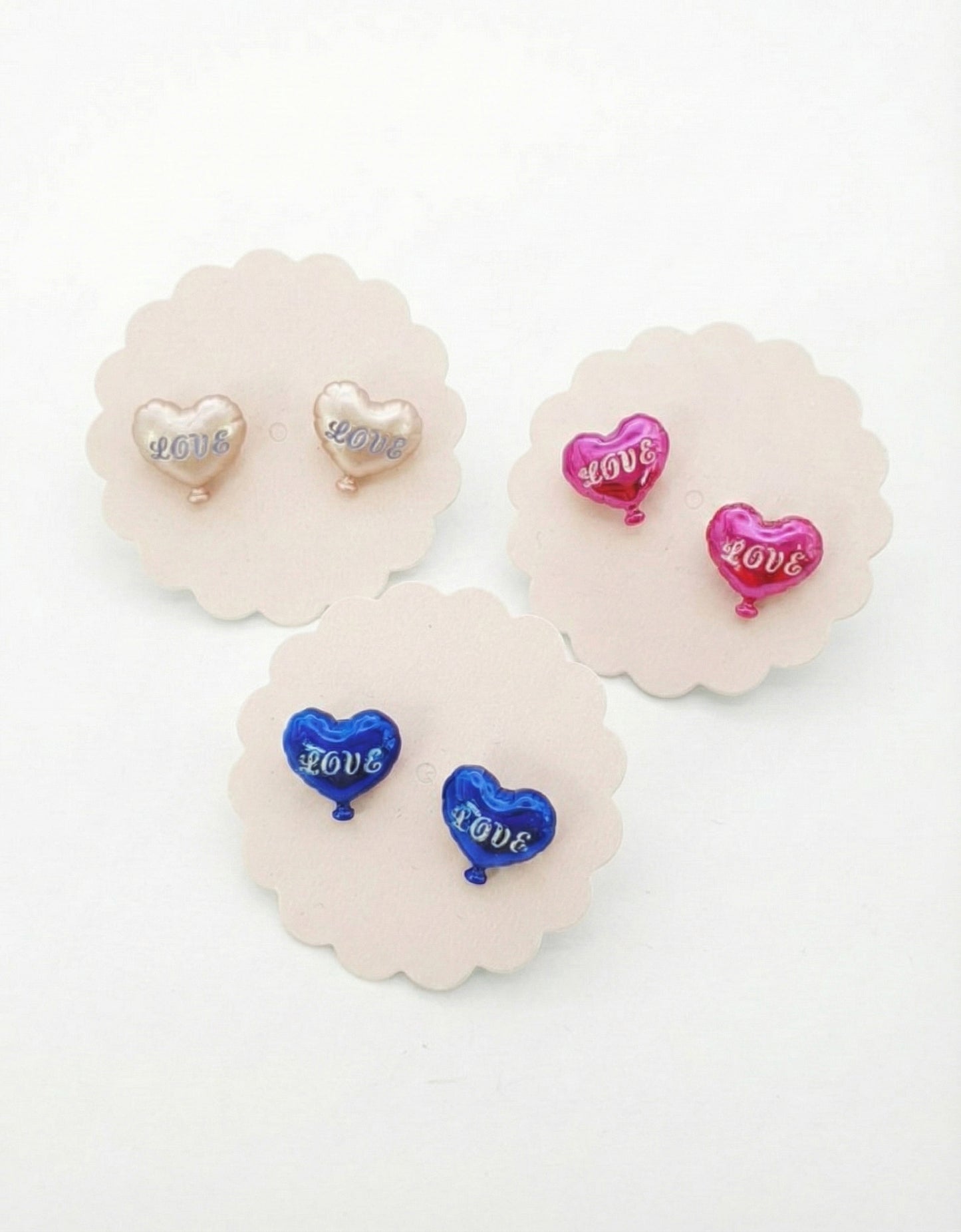Flat lay of three heart balloon earring pairs on white scalloped pads