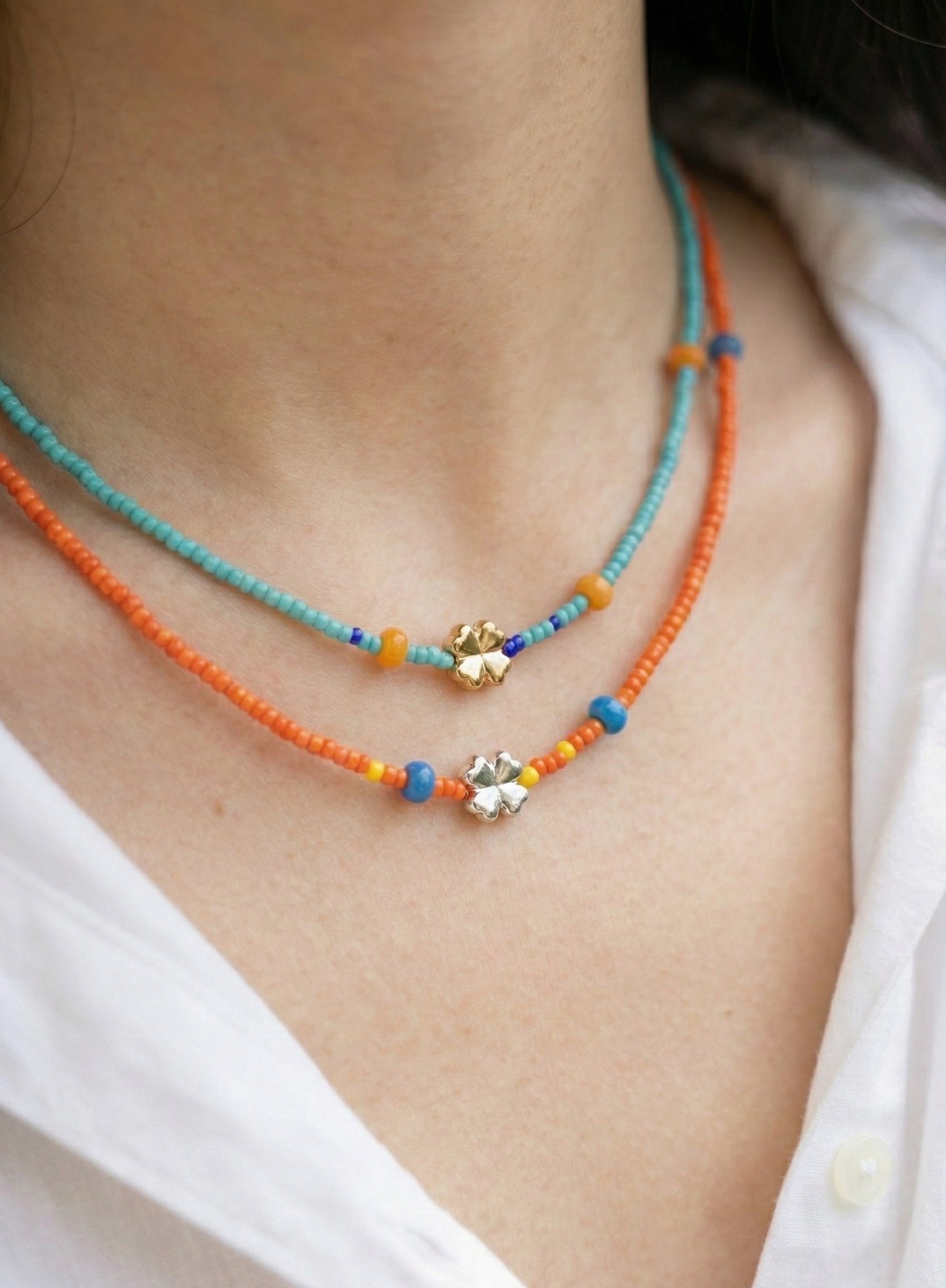 Neck close-up of woman wearing turquoise and orange layered seed bead choker necklaces with clover charms