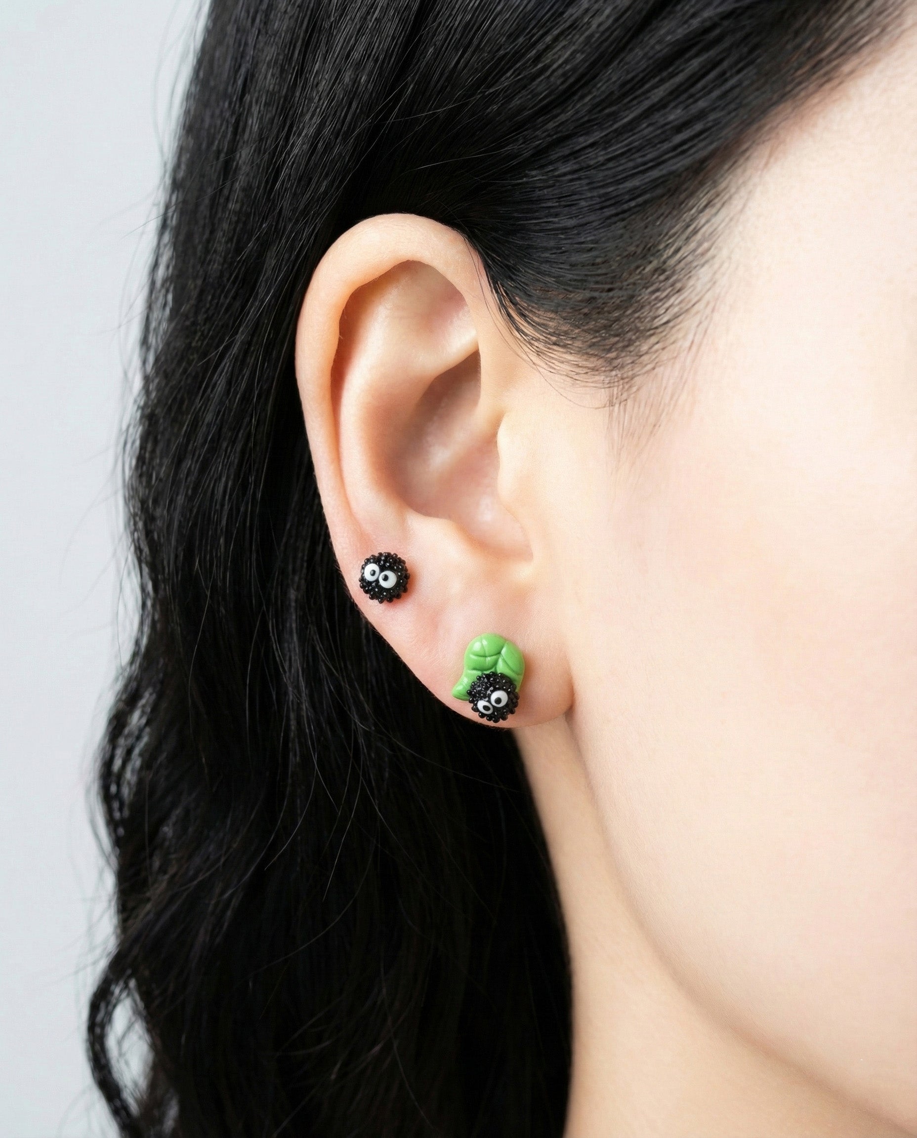 Side view of model ear wearing layered green leaf Soot Sprite earrings showing 3D sculptural detail