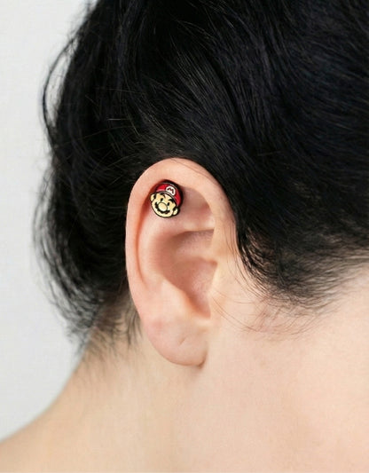 Mario face piercing worn on the upper ear of a model with black hair.